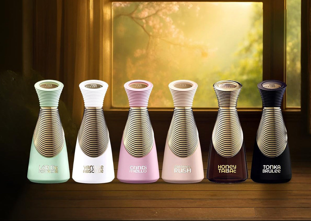 Set of six perfumes in different colors on a wooden surface with a blurred painting in the background.
